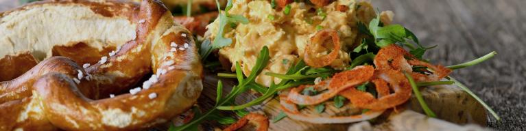 Bayerischer Obazter auf Rucolablättern mit Papikazwiebelringen und Brezel serviert Bayerischer Obazter auf Rucolablättern mit Papikazwiebelringen und Brezel serviert