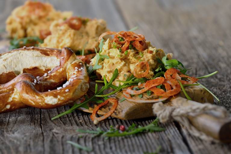 Bayerischer Obazter auf Rucolablättern mit Papikazwiebelringen und Brezel serviert